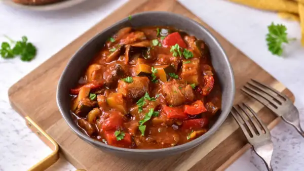 Aromaticzne leczo z pieczarkami, papryką i cukinią, podane w misce, ozdobione natką pietruszki.