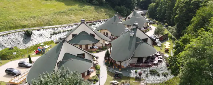 Malowniczy park zdrojowy Polańczyk z unikalnymi, zielonymi dachami budynków, placem zabaw i samochodami.